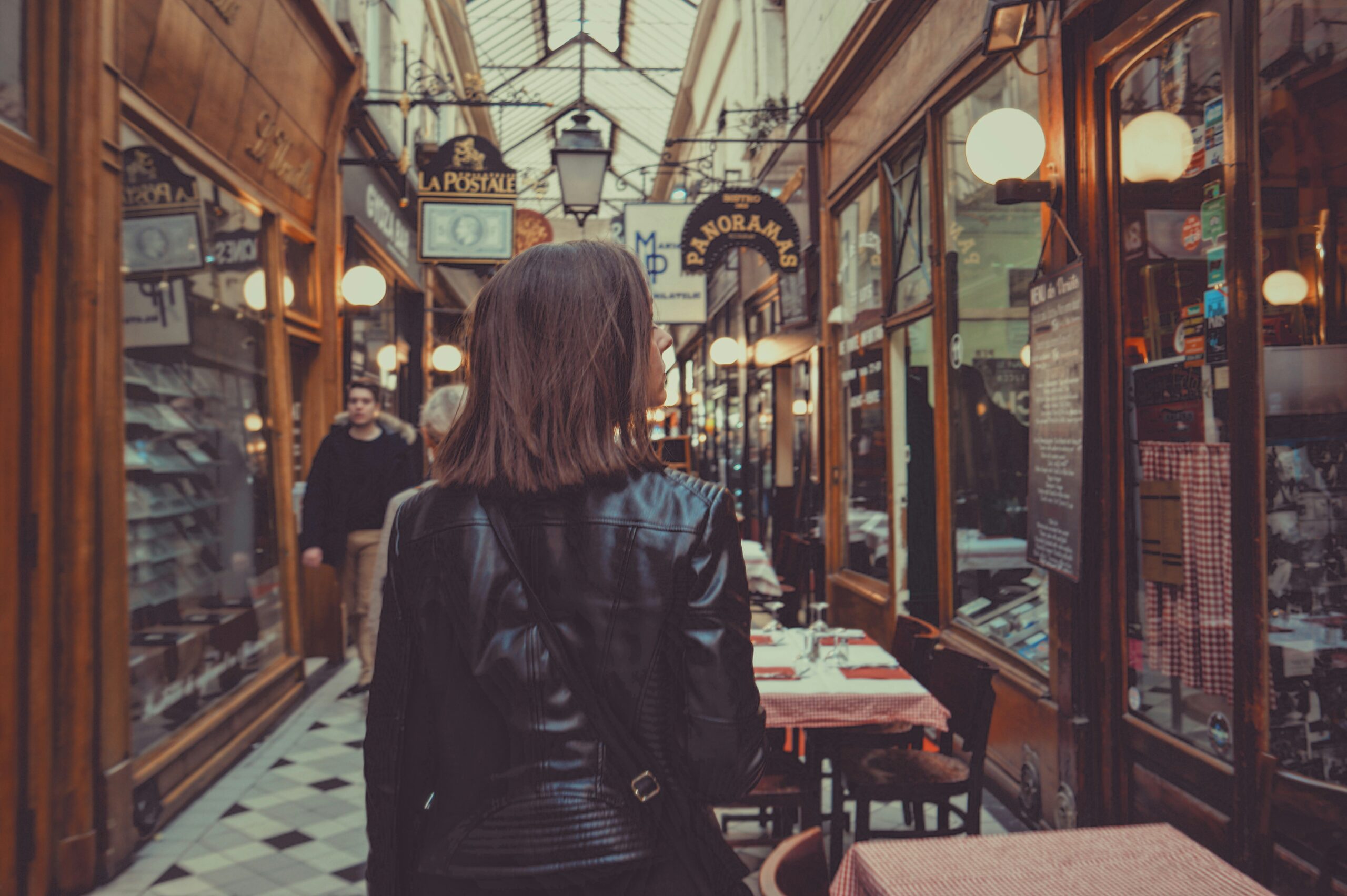 Woman in a leather jacket walking past shopfronts in a shopping area in Beeston, with various store displays and signage along the alleyway.